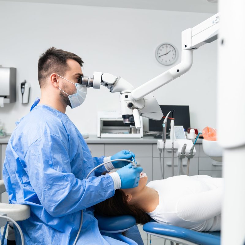 Young,Male,Dentist,Is,Examining,The,Patient's,Teeth,Under,A